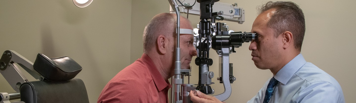 dr kamae examines the eyes of a male patient with a slit lamp during an exam spokane eye clinic